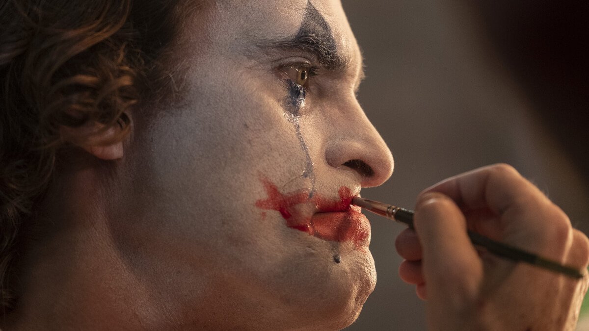 Joaquin Pheonix interprétant le Joker, se maquillant en pleurant dans le film "Joker" (2019) de Todd Phillips.